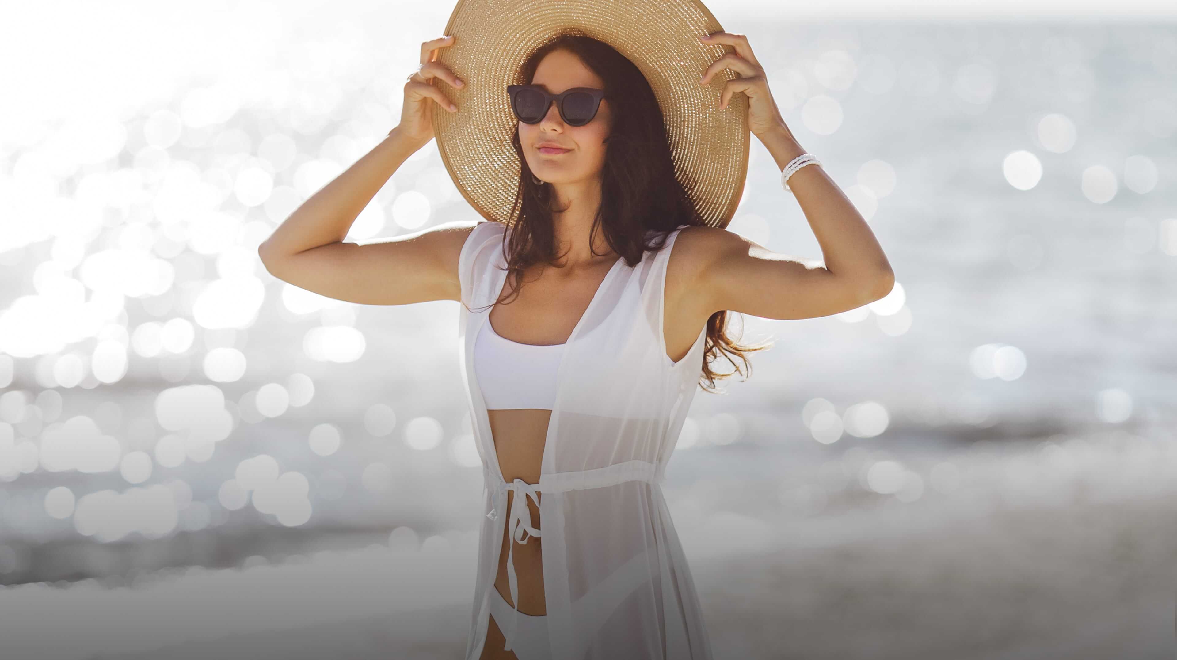 Woman on the beach holding her sun hat.