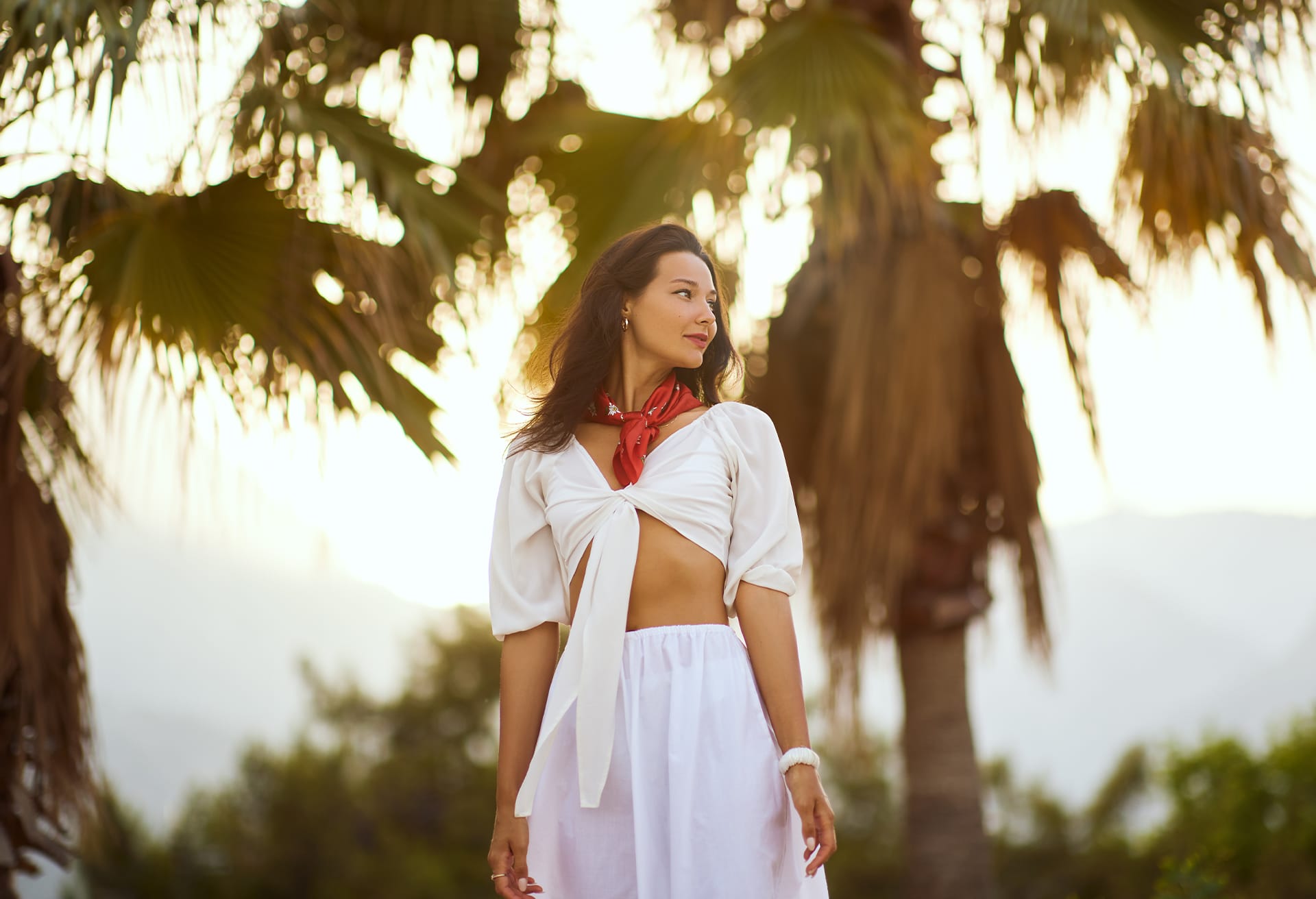 Woman with a red scarf tied around her neck with palm trees in the background