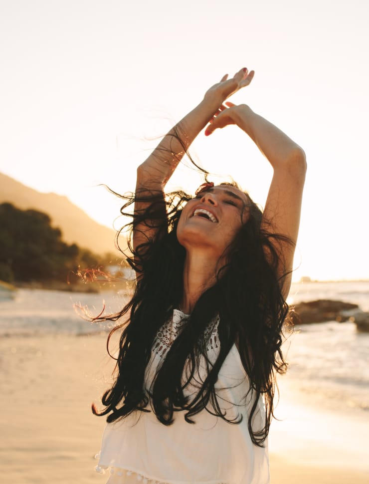 Dark-haired woman on the beach posing with her arms in the air