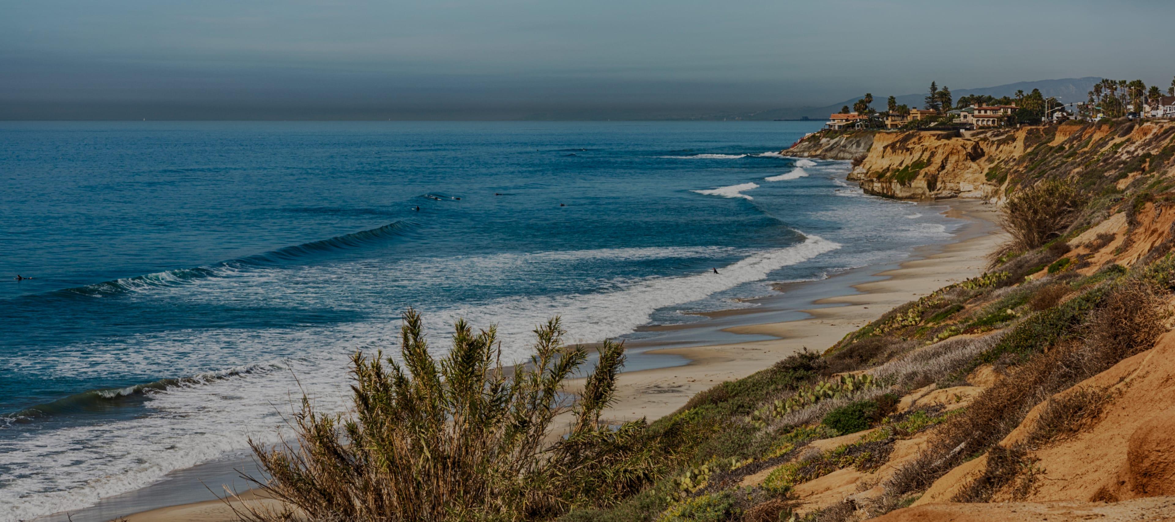 Coastal view with waves, sandy beach, and cliffs under a clear sky