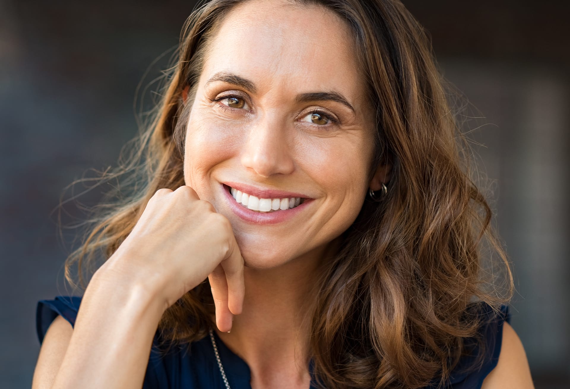 Smiling woman with wavy hair resting her chin on her hand
