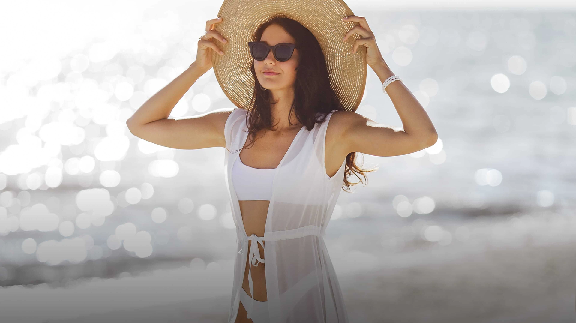 Woman in a white swimsuit and straw hat, standing by the water