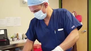 A healthcare professional in blue scrubs and a mask prepares equipment on a table