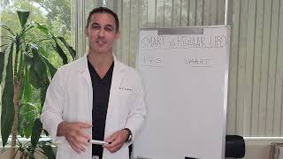 Man in a white coat standing near a whiteboard with writing. Plants in the background