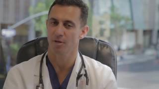 A doctor in a white coat, seated with a stethoscope around his neck