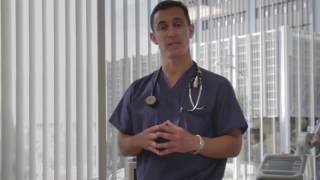 A medical professional in scrubs stands and speaks, with a stethoscope around their neck