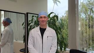 Person in surgical attire stands in a room with plants and mirrors