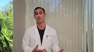 A person in a lab coat stands in front of a window with vertical blinds