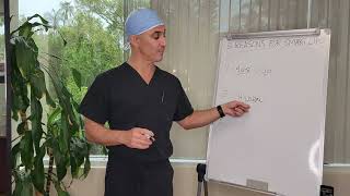 A person in scrubs and a cap points to a whiteboard with notes