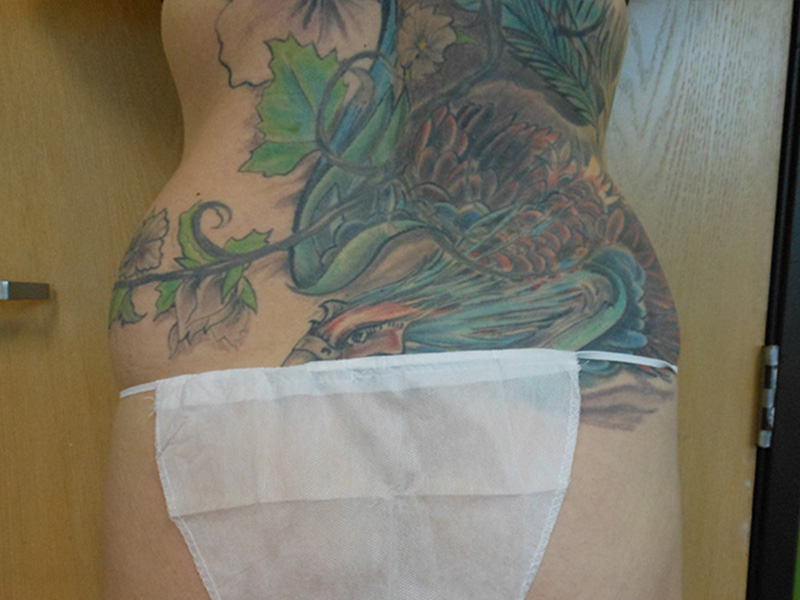 A torso with colorful tattoos and a white undergarment, against a wooden background