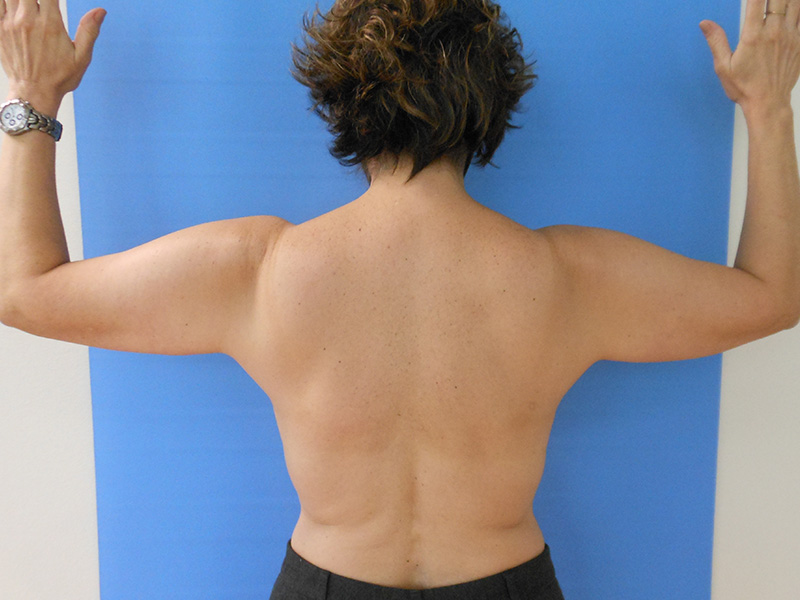 Person standing with arms raised, facing a blue background, showing their back