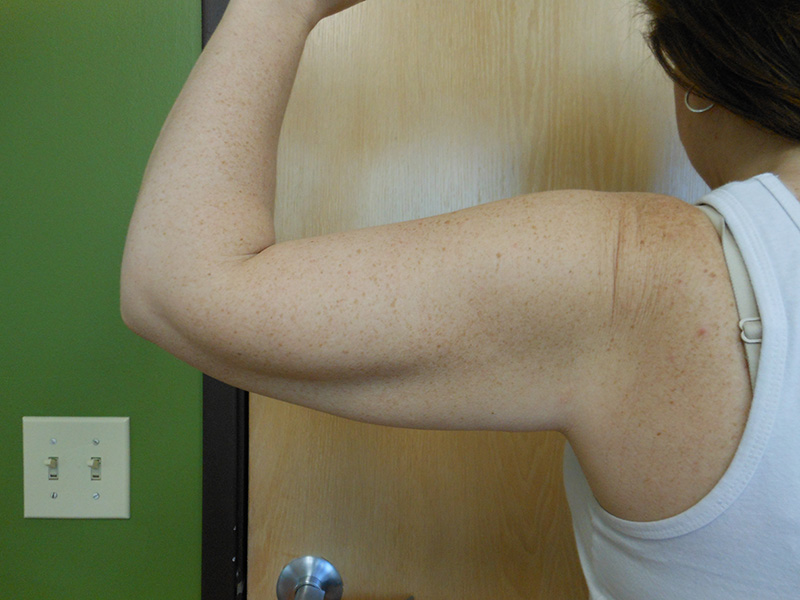 A person flexes their arm against a wooden door, showing muscle definition
