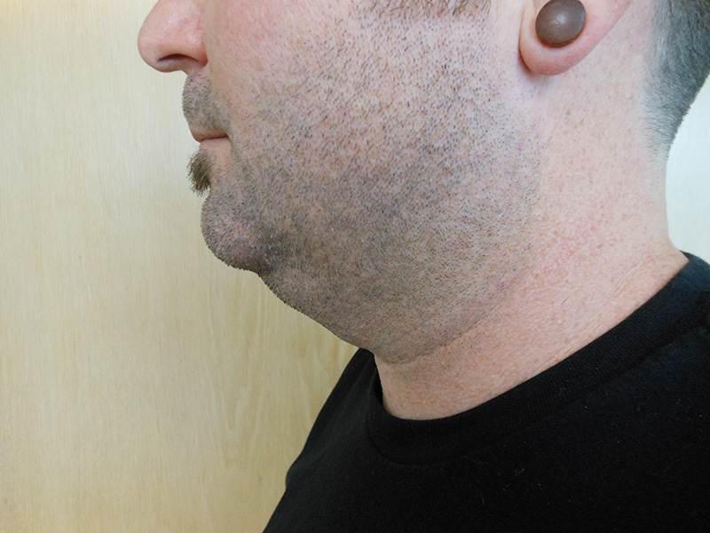 Profile view of a person with short hair and a plug in their ear, against a wooden background