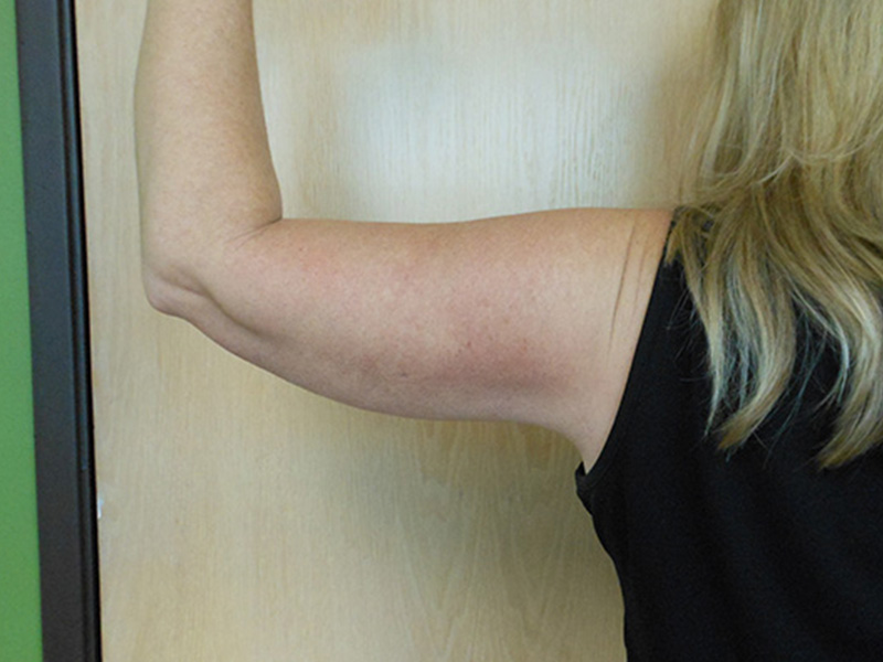 A close-up of a woman's arm flexing against a wooden wall
