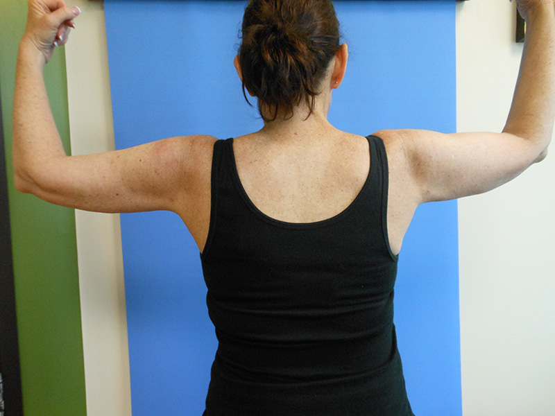 Person standing with arms raised, viewed from the back, against a blue background